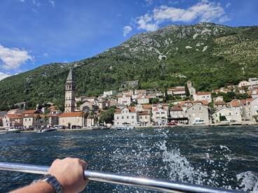 A scenic view of a charming coastal village with a historic church, captured from a boat, showcasing the stunning mountains and clear waters of the region.