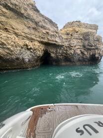 A scenic view of a boat approaching a rocky coastline with a cave entrance, showcasing the natural beauty of the area — perfect for exploring hidden gems on the water.