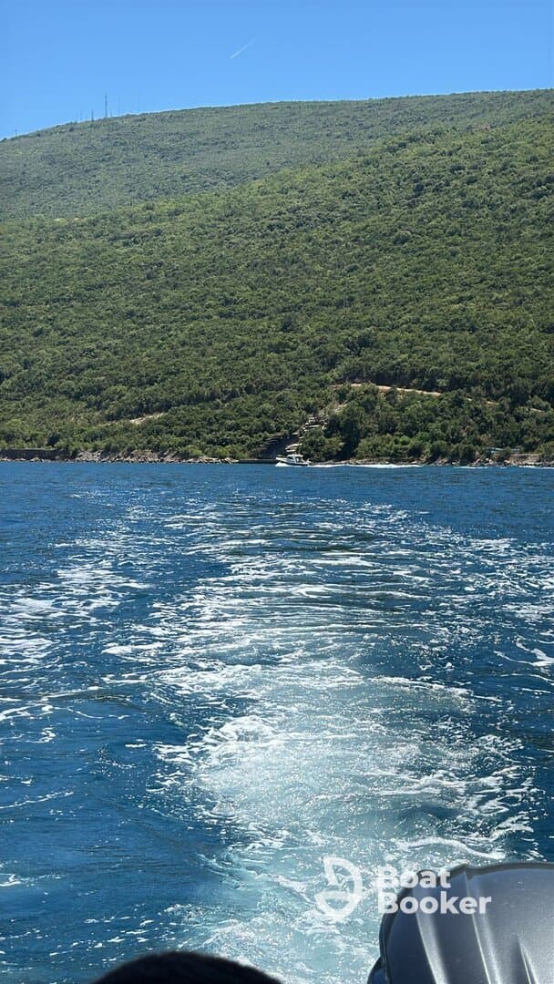 A scenic view of the coastline as the boat moves through clear waters, showcasing the lush greenery of the hills in the background.