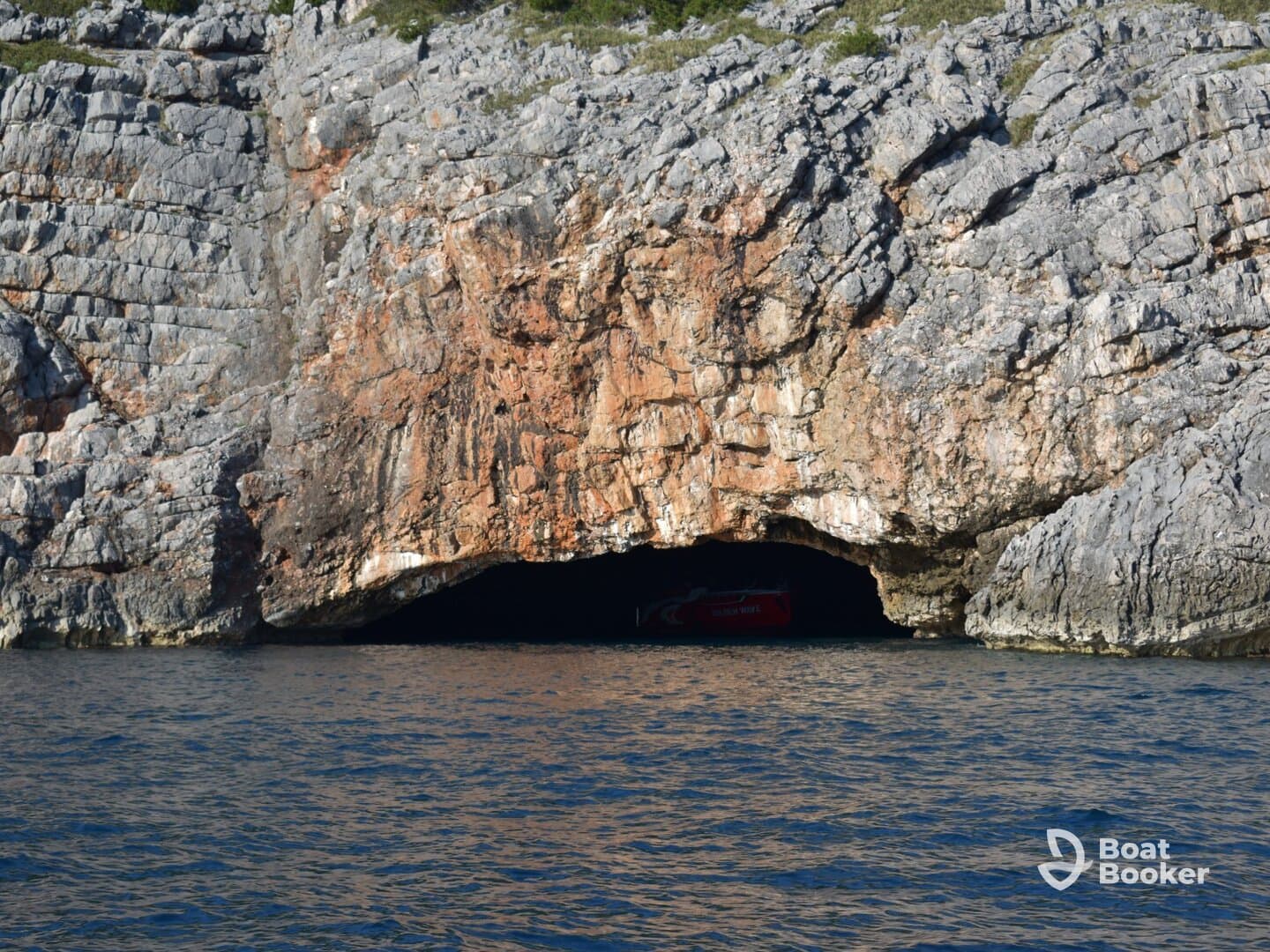A stunning view of a cave entrance along the coastline, with a boat partially visible inside — perfect for exploring hidden gems on the water.