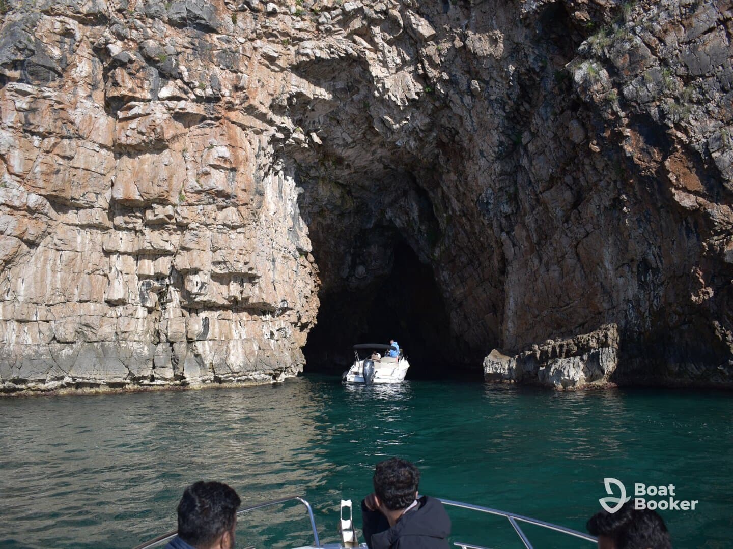 A thrilling boating adventure as guests explore a stunning cave entrance, surrounded by dramatic rock formations and crystal-clear waters.