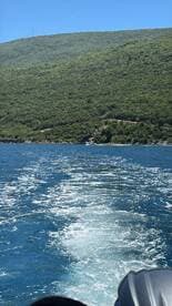 A scenic view of the coastline as the boat moves through clear waters, showcasing the lush greenery of the hills in the background.