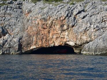 A stunning view of a cave entrance along the coastline, with a boat partially visible inside — perfect for exploring hidden gems on the water.