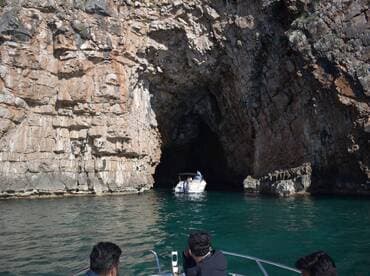 A thrilling boating adventure as guests explore a stunning cave entrance, surrounded by dramatic rock formations and crystal-clear waters.