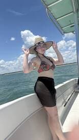 A young woman enjoys a sunny day on the boat, showcasing a fun summer vibe with clear skies and water in the background.