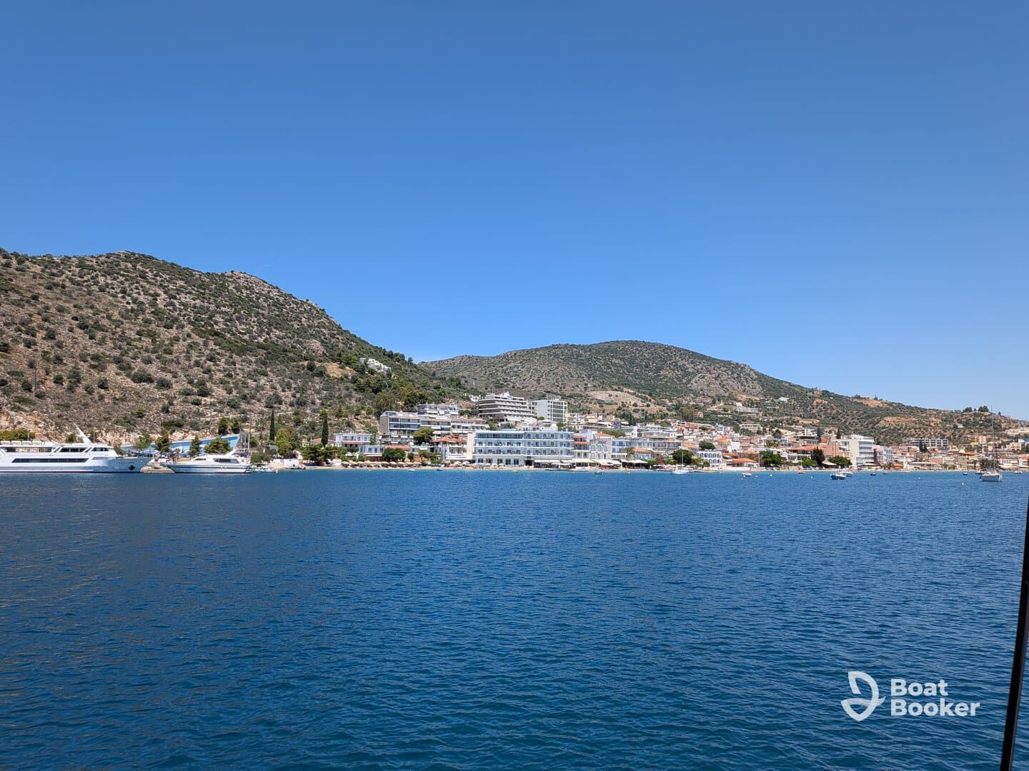 A picturesque view of a coastal town with lush hills and a serene harbor, showcasing the beauty of the landscape and inviting atmosphere for boating adventures.