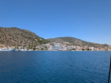 A picturesque view of a coastal town with lush hills and a serene harbor, showcasing the beauty of the landscape and inviting atmosphere for boating adventures.