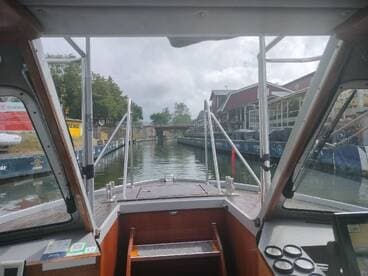 View from the helm of a boat navigating through a canal, showcasing the interior cabin and surrounding scenery.