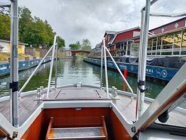 View from the bow of a boat navigating through a scenic canal, showcasing the charming waterfront buildings and lush greenery along the banks.