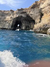 A stunning view of a boat navigating through a natural rock arch along a beautiful coastline, showcasing the breathtaking scenery of the area.
