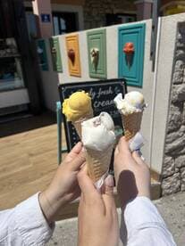 Three hands holding ice cream cones in front of a colorful backdrop, capturing a delightful moment of enjoying a sweet treat.