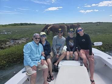 A family enjoys a day on the boat, with wild horses grazing in the background — a perfect blend of adventure and nature.