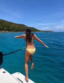 A woman joyfully jumps off the side of a boat into the vibrant blue waters, capturing the essence of summer fun and water adventures.