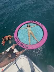A relaxing scene featuring friends enjoying a sunny day on the water, with one person lounging on a floating mat while others swim nearby — perfect for summer fun and aquatic adventures.