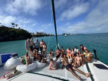 A lively group enjoys a day on a catamaran, soaking up the sun and celebrating together in the beautiful turquoise waters.