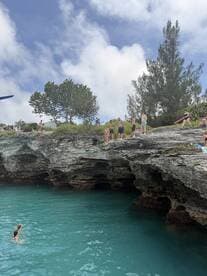 A lively group enjoys a day at the beach, with some swimming in the turquoise waters while others prepare to jump from the cliffs — a perfect scene for adventure seekers.