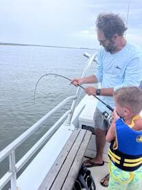 A father and son enjoy a fishing trip together on a boat, creating lasting memories on the water. The excitement of catching a fish adds to their adventure.