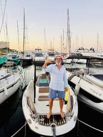 A man gives a thumbs up while standing on the deck of a boat in a marina, capturing the excitement of a day on the water.