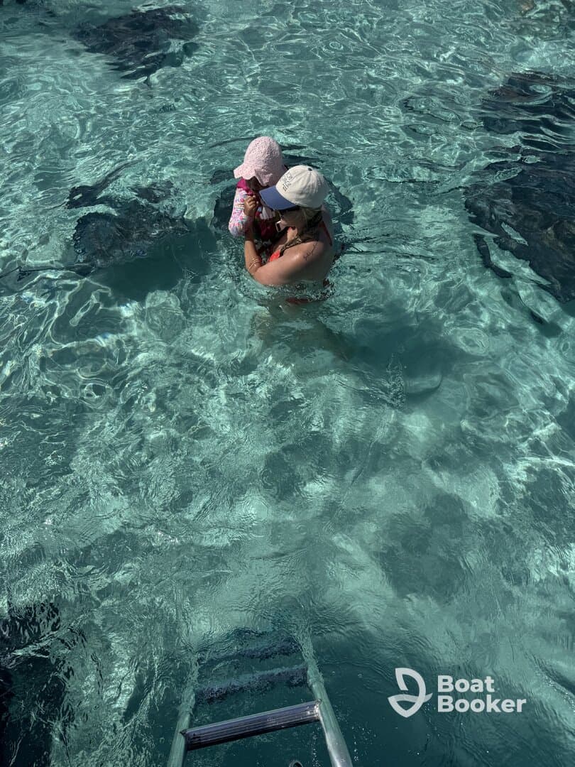 A mother holds her child while swimming with stingrays in crystal-clear waters, creating a memorable wildlife encounter perfect for family adventures.