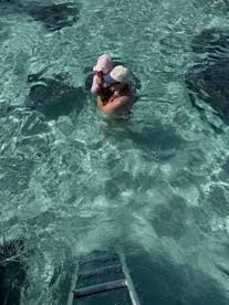 A mother holds her child while swimming with stingrays in crystal-clear waters, creating a memorable wildlife encounter perfect for family adventures.