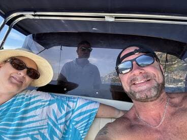 A couple enjoys a sunny day on the boat, capturing a cheerful selfie with stunning scenery in the background — perfect for memorable boating adventures.