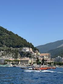 A scenic view of a small boat navigating along a picturesque coastline, showcasing the charming harbor and lush hills in the background — perfect for exploring coastal destinations.