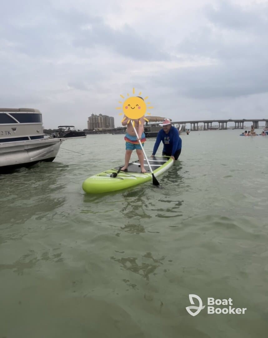 A child enjoys paddleboarding with an adult in shallow waters, showcasing a fun and engaging on-water activity perfect for family outings.