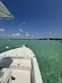 A scenic view from the bow of a boat, showcasing clear turquoise waters and people enjoying the sun and swimming — perfect for a day of fun on the water.