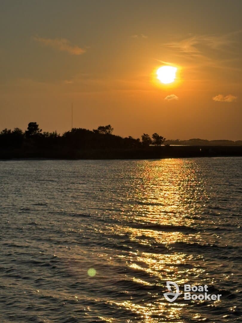 A stunning sunset casts golden reflections on the water, creating a picturesque scene perfect for evening boat cruises.