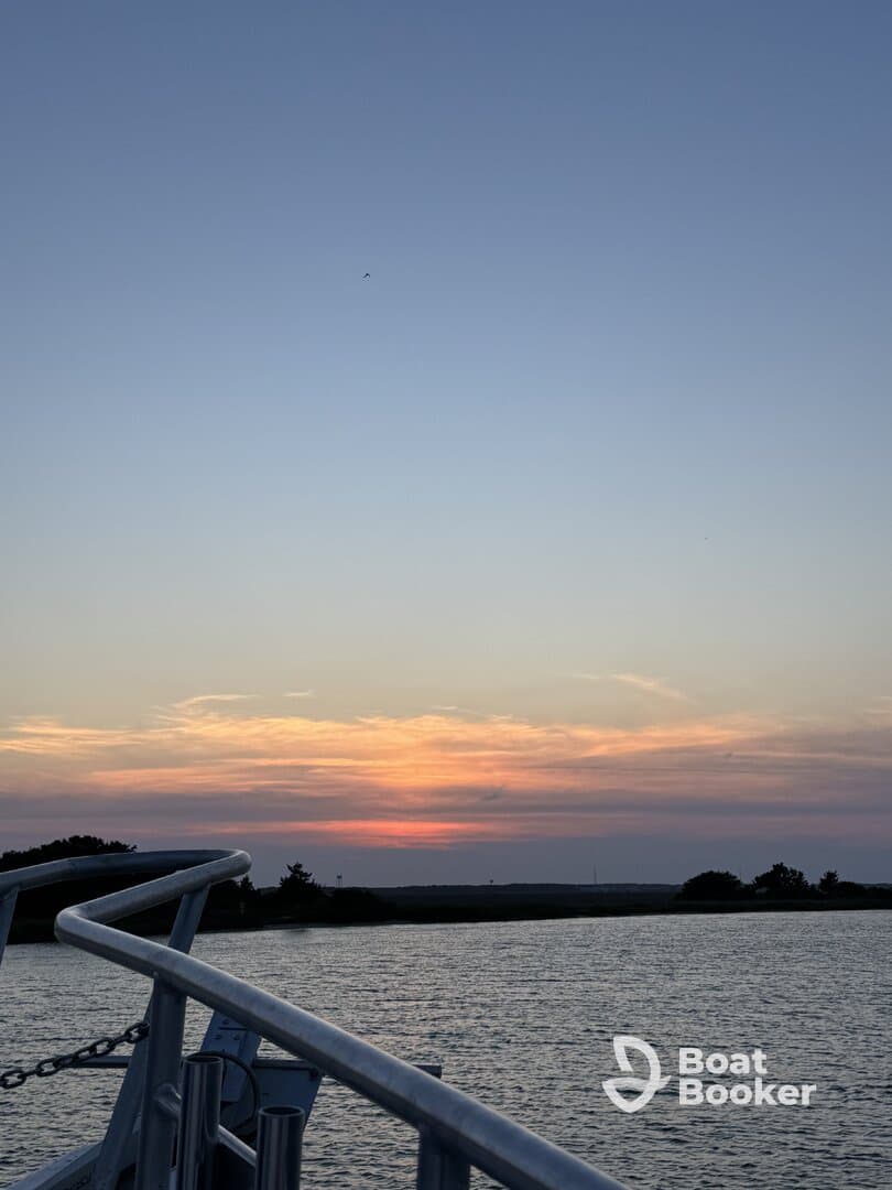 A serene sunset view from the deck of a boat, showcasing the tranquil waters and a hint of the boat's structure — perfect for evening cruises.