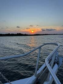 A serene sunset view from the bow of a boat, showcasing the tranquil waters and vibrant colors of the evening sky — perfect for romantic evening cruises.
