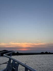 A serene sunset view from the deck of a boat, showcasing the tranquil waters and a hint of the boat's structure — perfect for evening cruises.