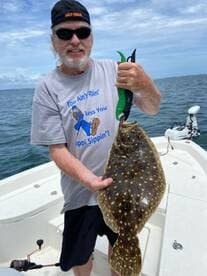 An enthusiastic angler proudly displays his catch of flounder while fishing aboard a boat — a perfect moment for fishing enthusiasts.