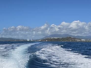 A stunning view of the coastline and mountains from a boat, showcasing the beautiful scenery and clear blue skies — perfect for a day on the water.
