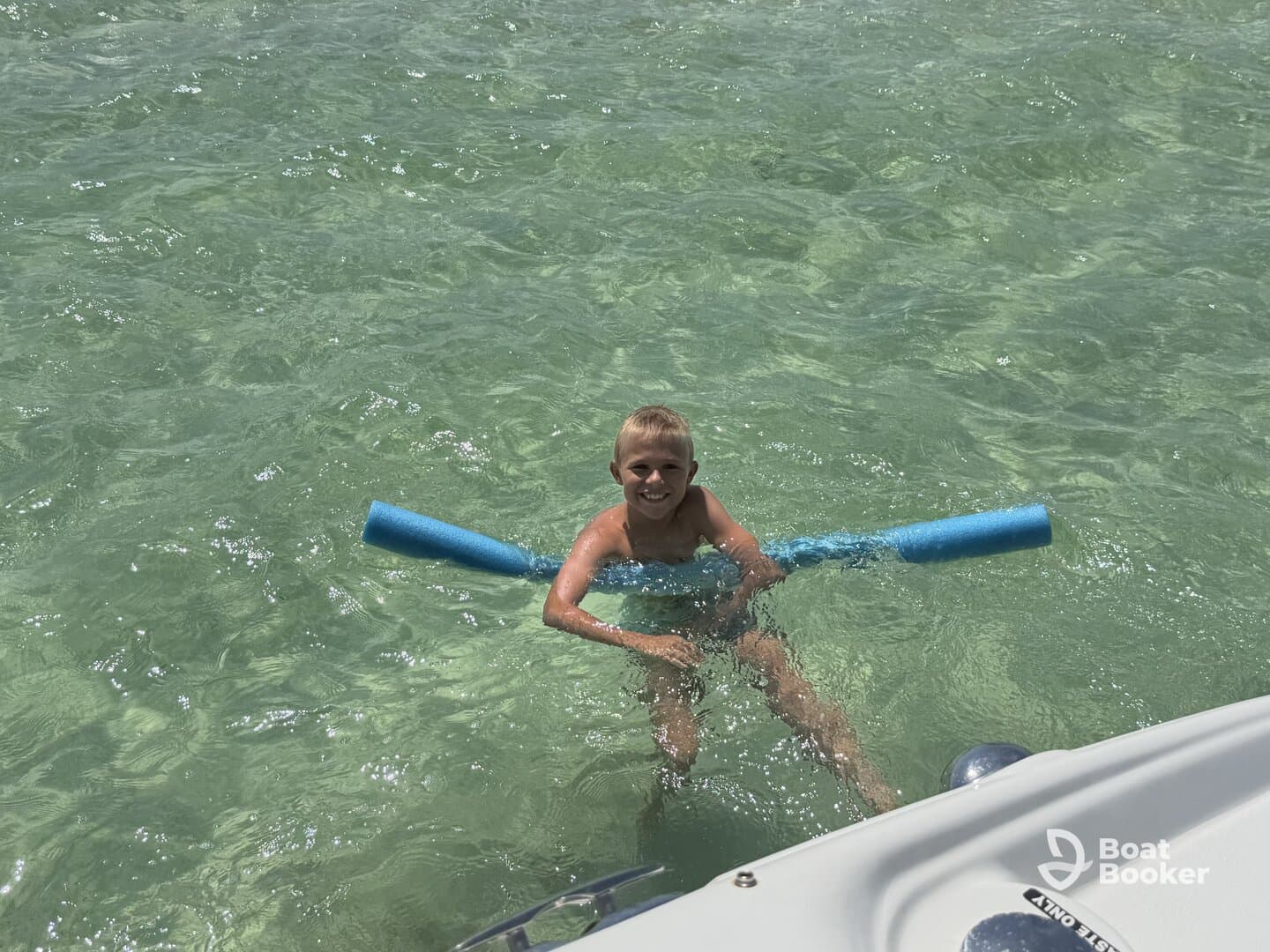 A joyful child plays in the clear waters, holding a pool noodle, showcasing the fun of a day on the water.