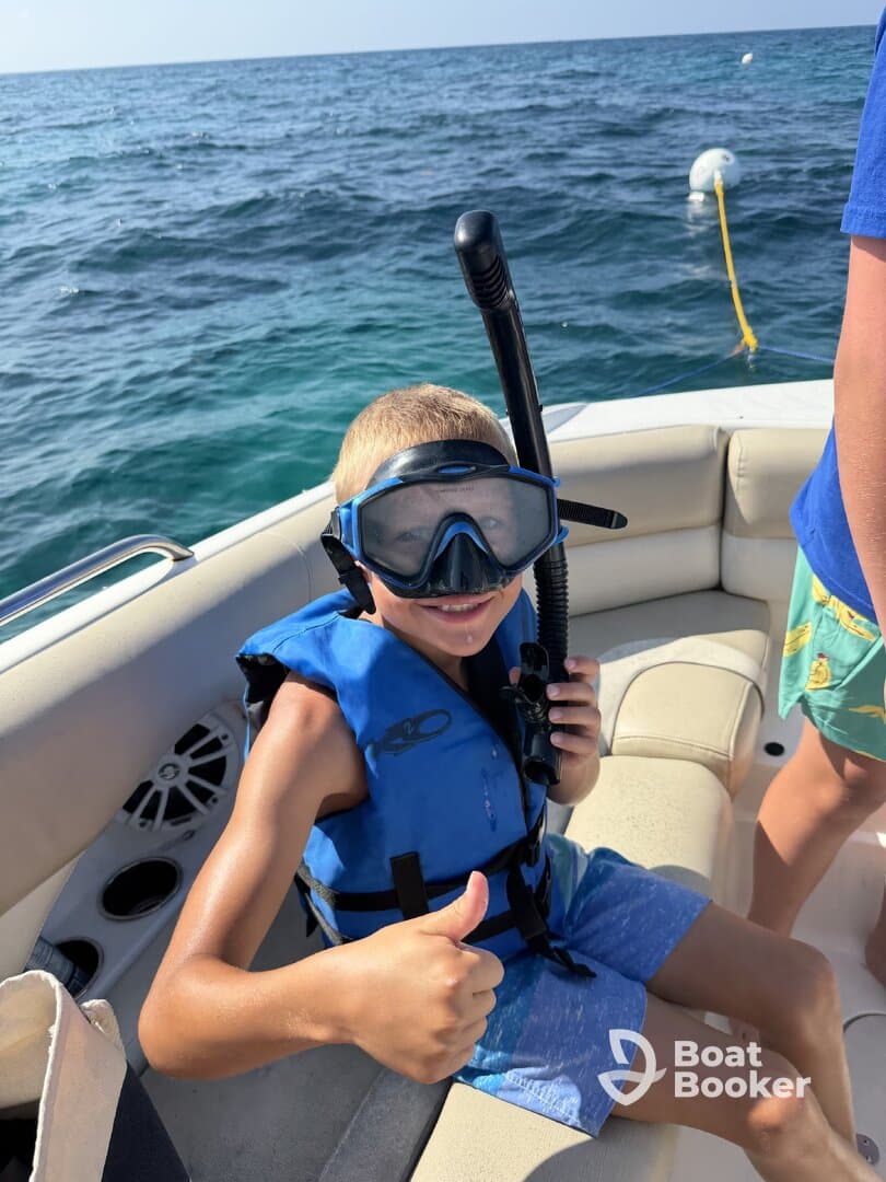 A young boy gives a thumbs up while preparing to snorkel on a boat, showcasing the excitement of underwater adventures.