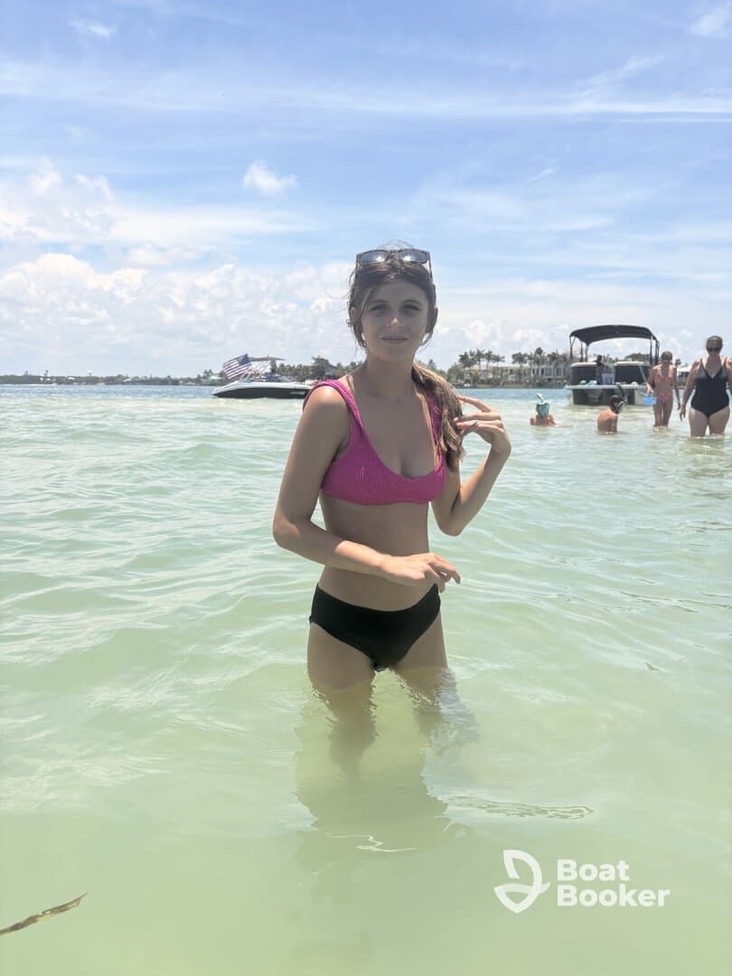 A young woman enjoys a refreshing swim in shallow waters, surrounded by friends and a beautiful beach backdrop — perfect for summer fun and relaxation.