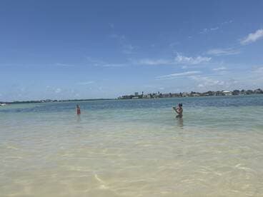 Two individuals enjoy a sunny day at the beach, wading in the shallow waters — a perfect setting for family fun and relaxation.