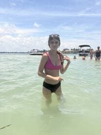A young woman enjoys a refreshing swim in shallow waters, surrounded by friends and a beautiful beach backdrop — perfect for summer fun and relaxation.