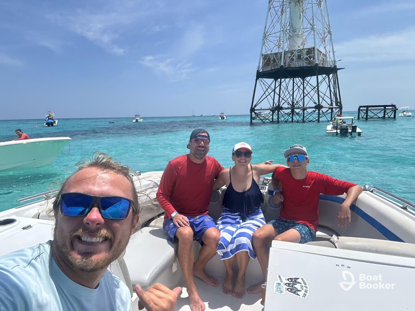 A cheerful group enjoys a sunny day on the boat, capturing memories against the backdrop of a beautiful ocean and a lighthouse. Perfect for snorkeling adventures and fun on the water.
