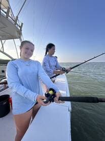 Two young girls enjoy a fishing trip on a boat, showcasing the excitement of angling in the open ocean — a perfect family adventure.
