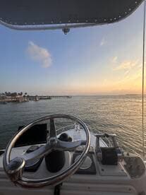 A view from the helm of a boat, showcasing the steering wheel and control panel against a serene sunset backdrop over the water.