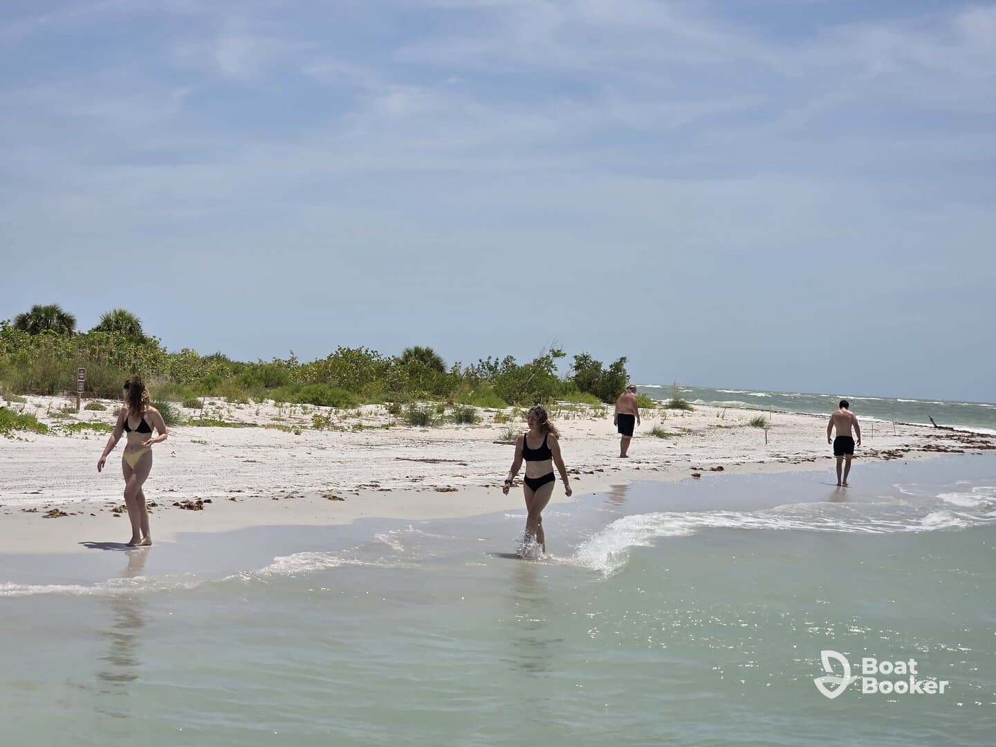 A group of friends enjoys a sunny day at the beach, walking along the shore and wading in the gentle waves — an ideal setting for relaxation and fun in the sun.