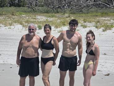 A cheerful family poses together on the beach, enjoying a sunny day by the water — perfect for creating lasting memories during summer vacations.