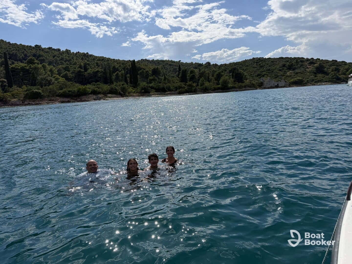 A joyful group enjoys a refreshing swim in the clear waters, surrounded by lush greenery and a picturesque coastline — perfect for summer adventures.