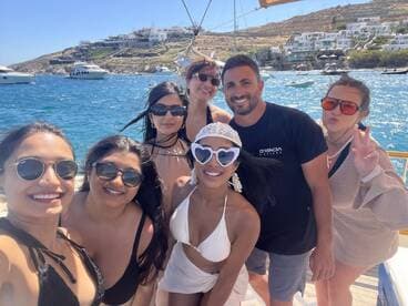 A joyful group of friends poses for a selfie on a boat in Mykonos, capturing the essence of summer fun and celebration on the water.