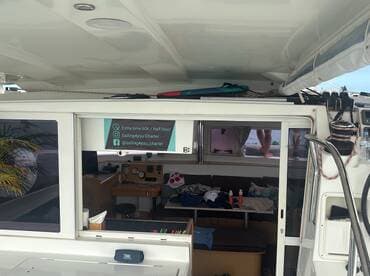 Inside view of a catamaran's cabin showcasing the helm and seating area, with contact information for charter services visible.