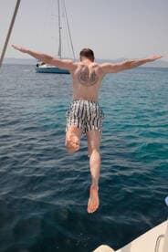 A man joyfully leaps into the crystal-clear waters from a sailboat, capturing the essence of summer fun and water activities.