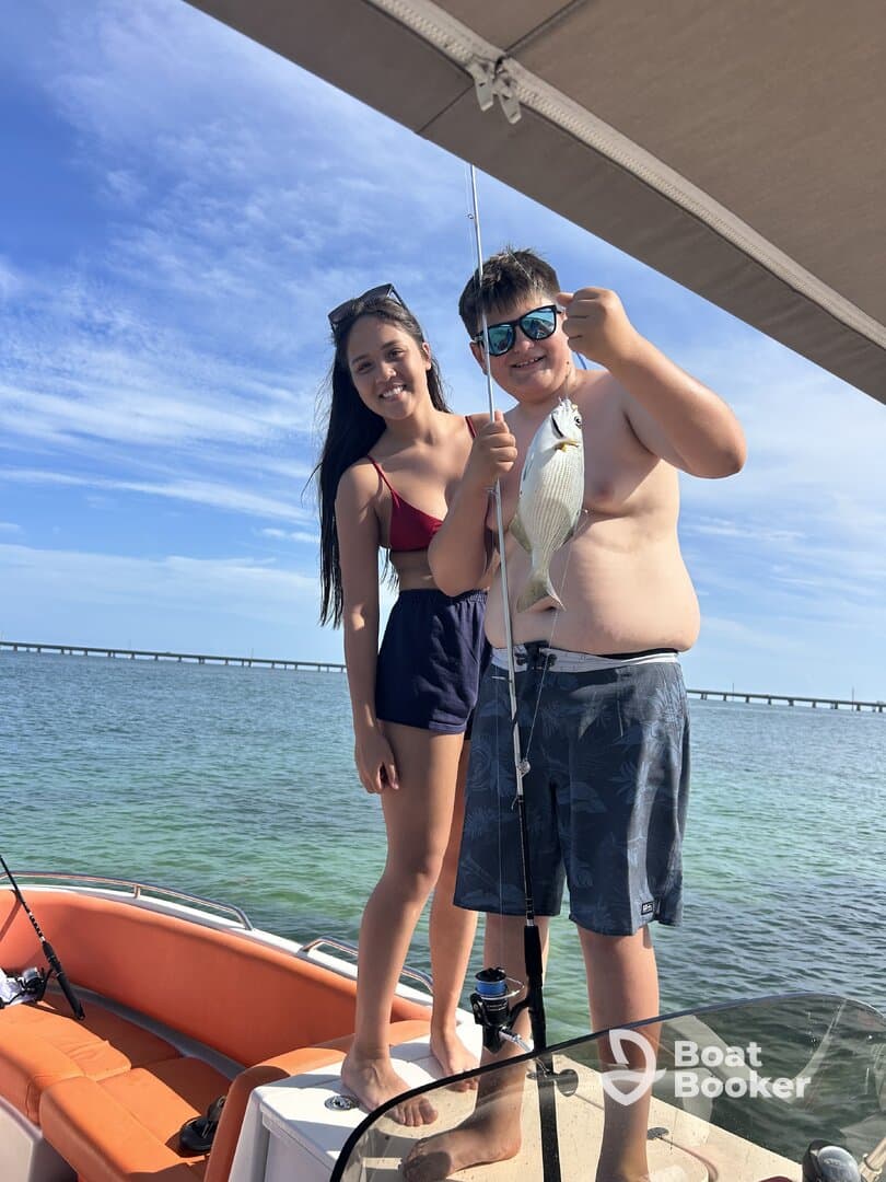 Two kids proudly display their catch while fishing on a boat, capturing a joyful moment of adventure on the water.