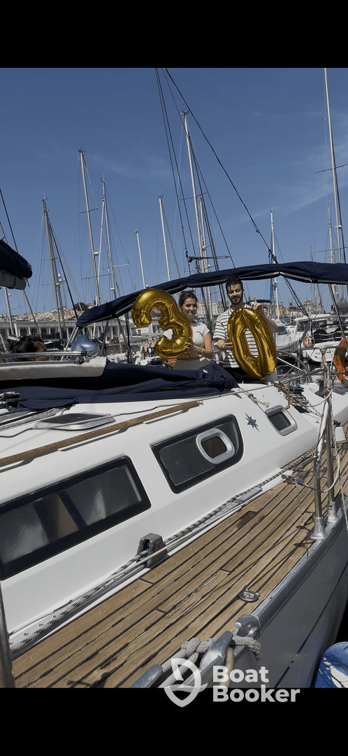 A couple celebrates a 30th birthday aboard a yacht, holding festive balloons against a backdrop of sailboats in the marina.